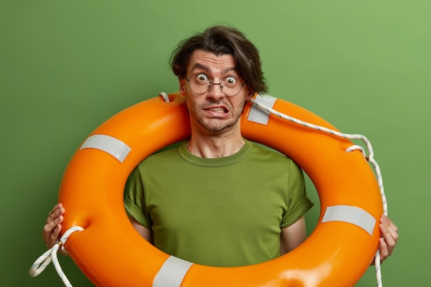 Photo gratuite un sauveteur inquiet serre les dents et semble perplexe, pose avec un équipement de sécurité de natation, porte une bouée de sauvetage en caoutchouc, se dresse