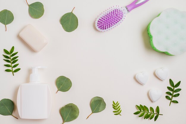 Savon; brosse à cheveux; bouteille de distributeur et feuilles vertes sur fond blanc