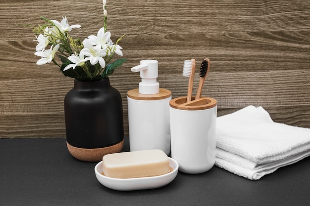 Savon; brosse à dents; bouteille cosmétique; serviette et vase de fleurs blanches sur une surface noire