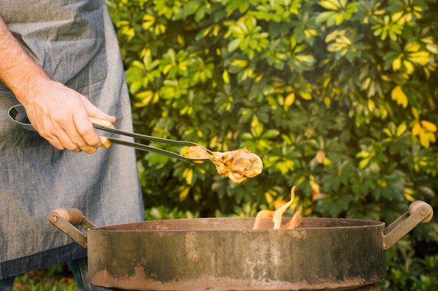 Savoureuse viande grillée dans des pinces métalliques sur la grille du feu à la main