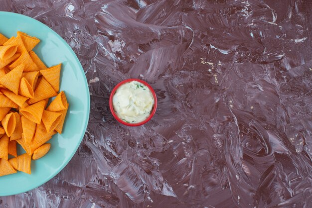 De savoureuses chips épicées sur une assiette à côté de yaourt, sur la table en marbre.