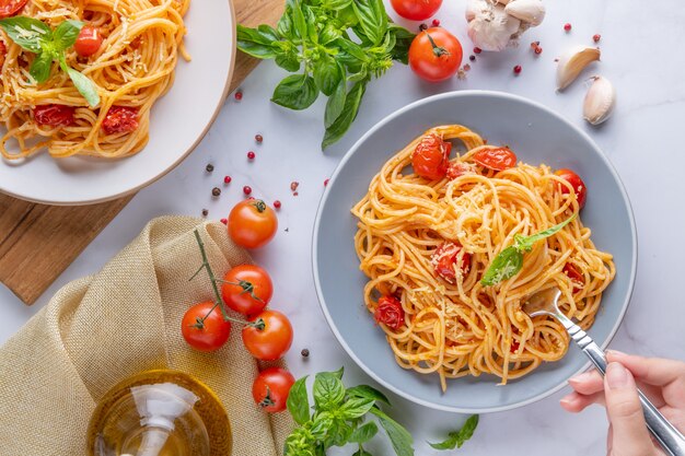 Savoureuses pâtes spaghetti italiennes classiques appétissantes avec sauce tomate, fromage parmesan et basilic sur assiette et ingrédients pour la cuisson des pâtes sur une table en marbre blanc. Espace de copie de vue de dessus à plat.