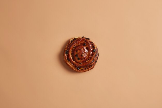 Savoureux petit pain moelleux en spirale ronde feuilletée avec des raisins secs cuits dans une boulangerie. Produit de boulangerie à haute teneur en calories contenant beaucoup de matières grasses et de sucre. Rouleau maison sur fond de studio beige. Concept de nourriture sucrée.