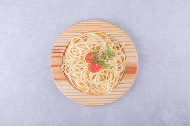 De savoureux spaghettis bouillis aux tomates sur une plaque en bois.