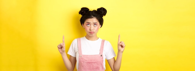 Photo gratuite sceptique adolescente asiatique avec maquillage rose glam pointant et regardant vers le haut relucta debout non amusé