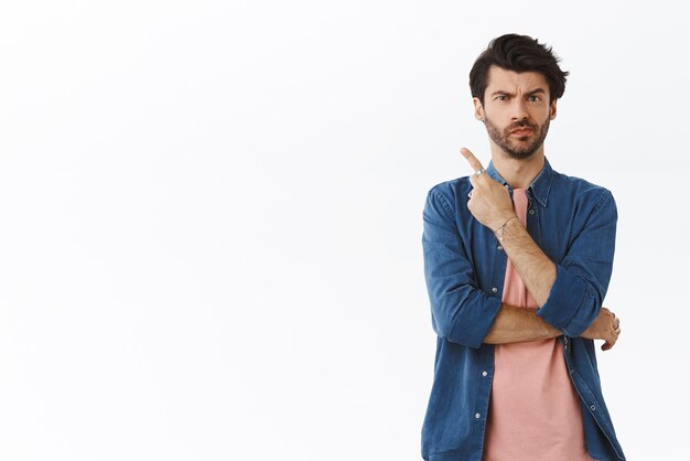 Sceptique incertain bel homme en t-shirt rose grimace fronçant les sourcils pensif et incertain ont des doutes pointant le coin supérieur gauche pas sûr d'acheter ou de ne pas demander de conseils en pensant et en hésitant