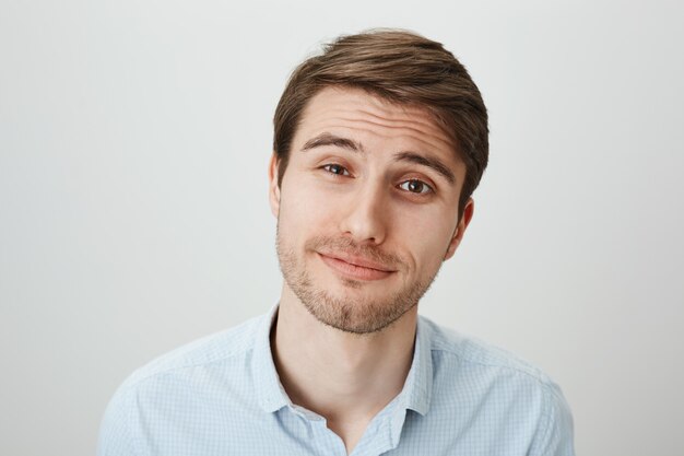 Sceptique jeune homme souriant et levant les sourcils incrédulité