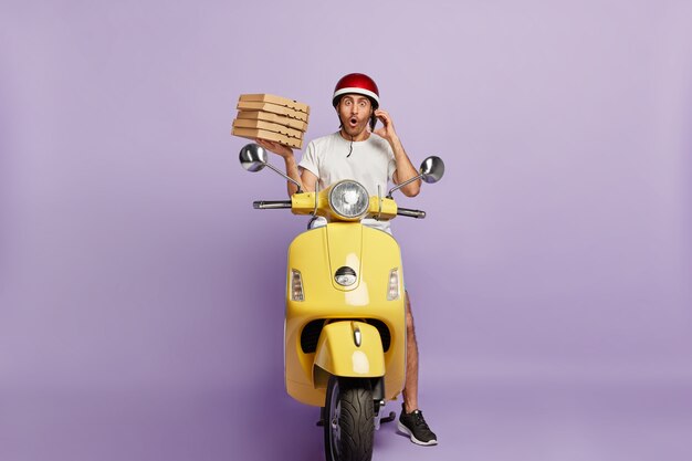 Scooter de conduite de livreur choqué tout en tenant des boîtes de pizza