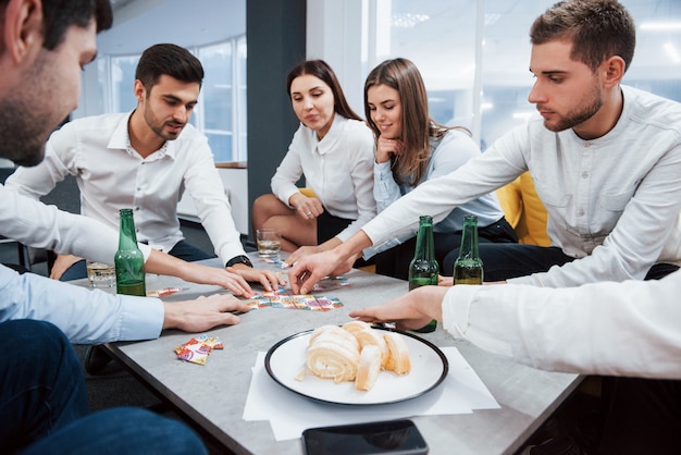 Photo gratuite se détendre avec du gibier. célébration d'une transaction réussie. jeunes employés de bureau assis près de la table avec de l'alcool