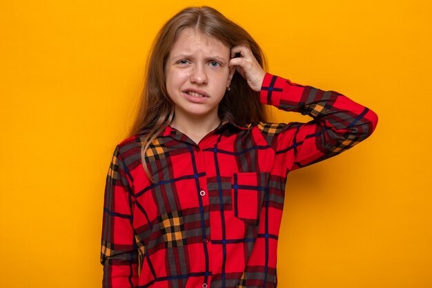 Se gratter la tête confuse belle petite fille portant une chemise rouge