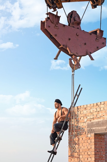 Se reposer un peu. Hunky constructeur torse nu assis sur une échelle au gratte-ciel en construction