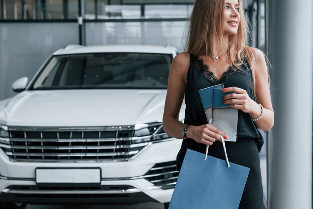 Se sentir bien. Fille et voiture moderne dans le salon. Le jour à l'intérieur. Acheter un véhicule neuf