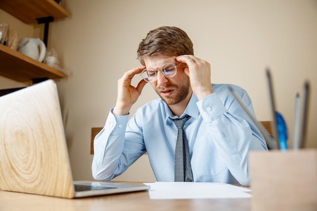 Se sentir malade et fatigué. Frustré triste malheureux jeune homme malade massant sa tête alors qu'il était assis à son lieu de travail au bureau.