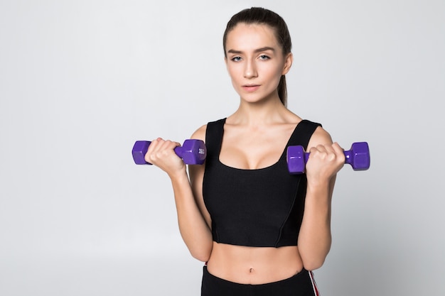 Séance d'entraînement de fitness femme souriante avec de petits haltères isolés sur un mur blanc