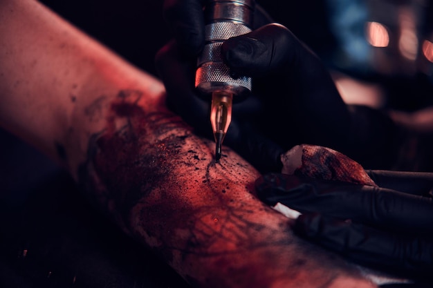 Photo gratuite séance photo en gros plan de la fabrication de tatouages, l'artiste travaille avec une machine à tatouer sur la main du client.