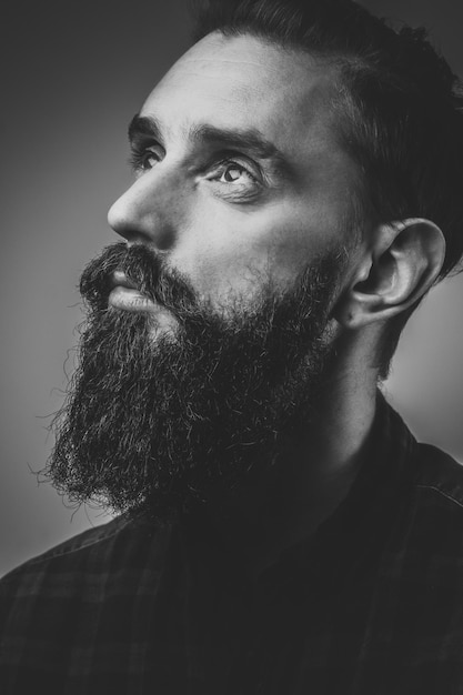 Séance photo en gros plan d'un homme pensif avec barbe, photo en noir et blanc à faible contraste.