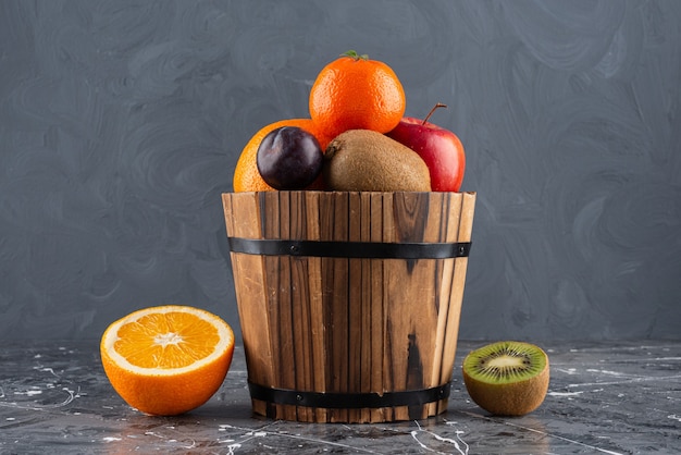 Seau en bois plein de fruits frais sur une surface en marbre.