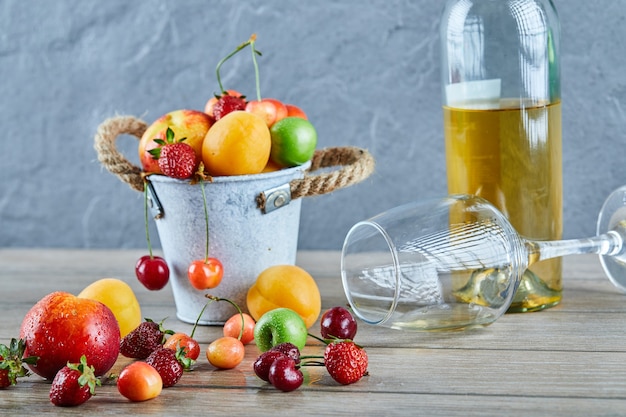 Seau de fruits frais d'été, bouteille de vin blanc et verre vide sur table en bois.