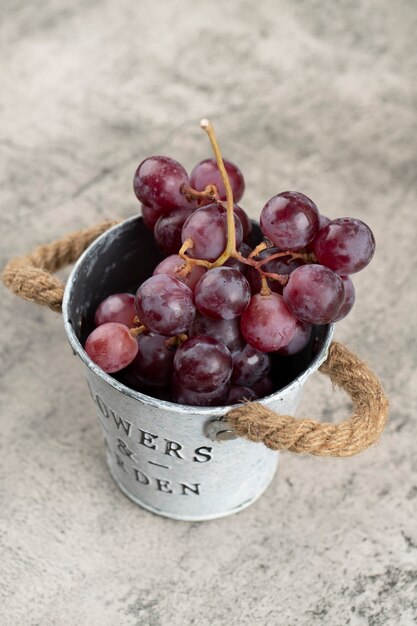 Seau en métal de raisins rouges juteux sur fond de pierre.