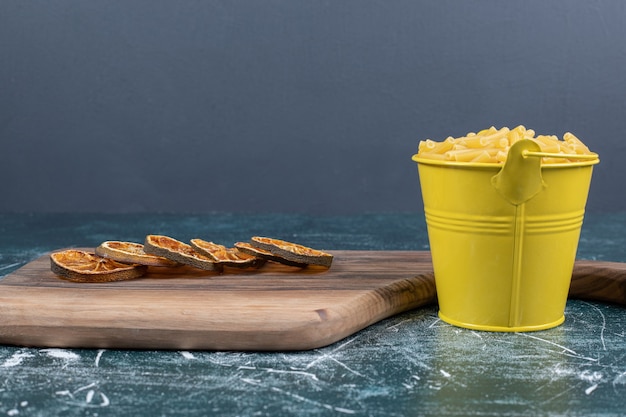 Seau de pâtes penne et tranches d'orange sur fond bleu. Photo de haute qualité