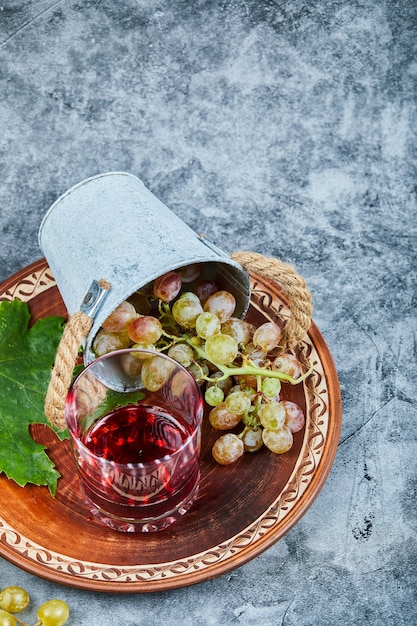 Seau de raisins et un verre de jus sur marbre.