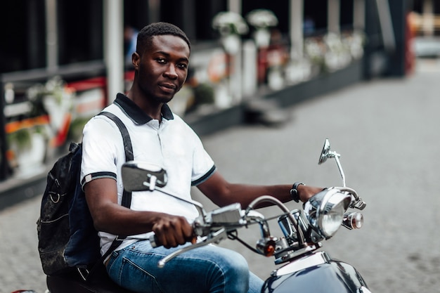 Sécher les cours. Étudiant masculin attrayant assis sur une moto dans la rue.