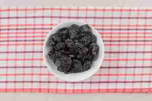 Photo gratuite sécher les prunes noires dans une tasse en céramique sur du béton.