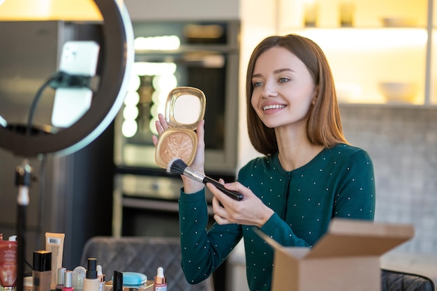 Les secrets d'un bon maquillage. Jolie jeune femme en robe verte montrant des conseils de maquillage