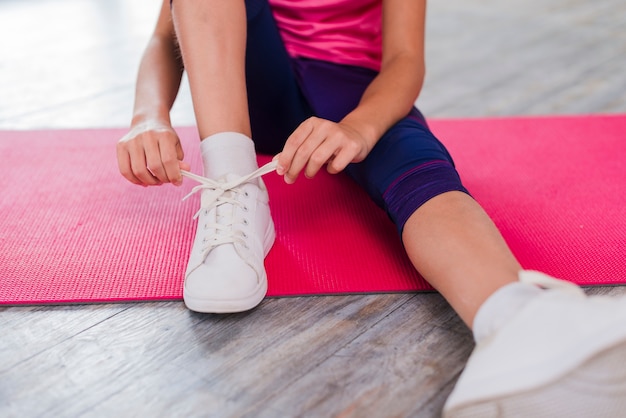 Section basse d&#39;une fille assise sur un tapis d&#39;exercice nouant des lacets