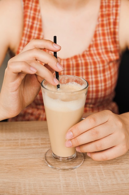 Section médiane d&#39;une femme assise dans un café tenant une paille et une tasse de café au lait