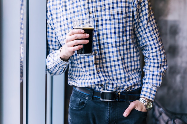 Section médiane d&#39;un homme avec sa main dans la poche tenant le verre à bière