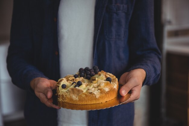 Section médiane de l'homme tenant un gâteau aux myrtilles dans la salle de séjour