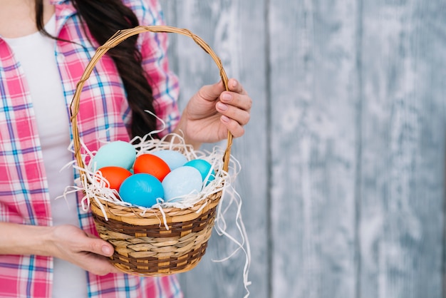 Photo gratuite section médiane de la main de la femme tenant des oeufs de pâques colorés dans le panier contre un arrière-plan flou