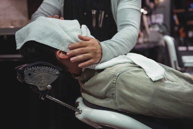 Section médiane sur le visage des clients essuyant le coiffeur avec une serviette chaude