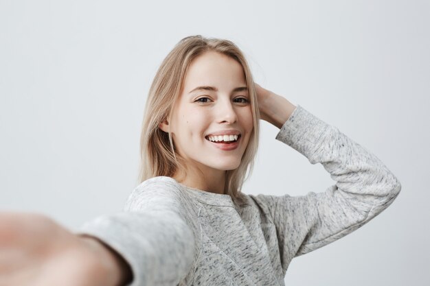 Séduisante femme blonde aux yeux noirs habillée avec désinvolture ayant un look ravissant souriant largement. Belle femme ayant une expression gaie tout en posant