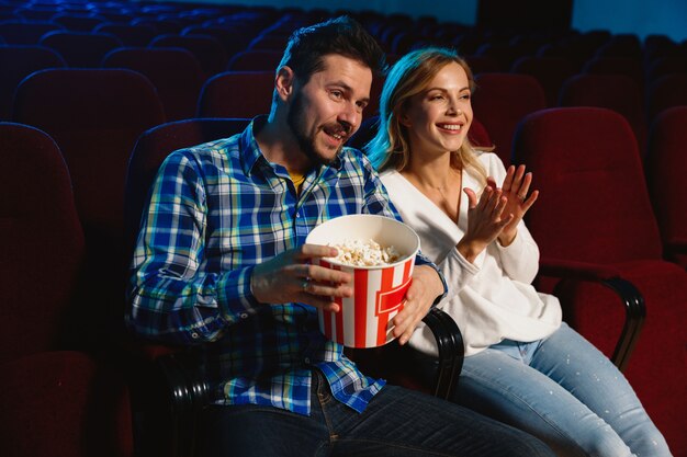 Séduisante jeune couple caucasien regardant un film dans un cinéma, une maison ou un cinéma. Ayez l'air expressif, étonné et émotif. S'asseoir seul et s'amuser. Relation, amour, famille, week-end.