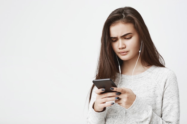 Séduisante Jeune Femme Avec Une Expression Inquiète Tient Le Téléphone Et écoute De La Musique