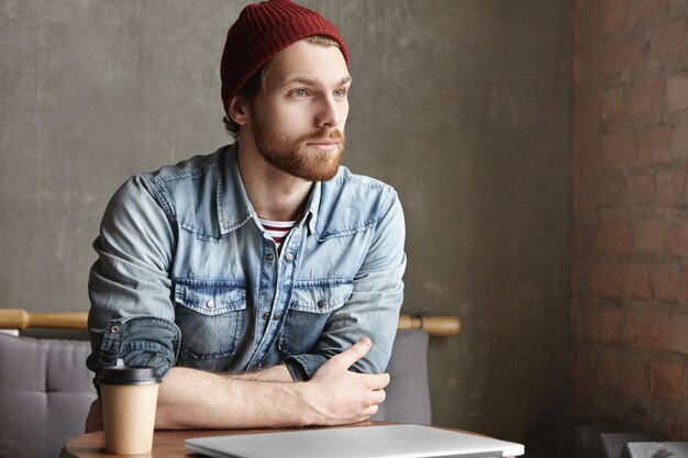 Séduisante jeune hipster caucasien dans des vêtements élégants ayant un look rêveur réfléchi