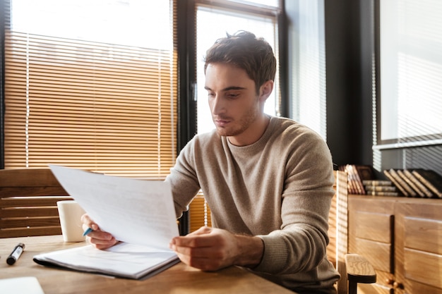 Séduisante jeune homme au bureau travaillant avec des documents.