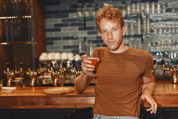 Séduisante jeune homme debout derrière le bar. L'homme dans un T-shirt marron tient un verre dans ses mains.