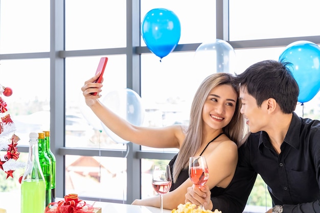 Séduisante jeune homme et femme célèbrent Noël et le Nouvel An dans une fête de bureau homme et femme prenant selfie ensemble