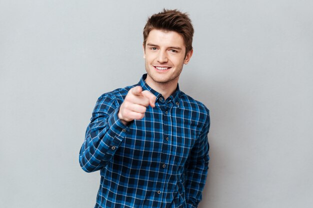 Séduisante jeune homme heureux debout sur un mur gris et pointant