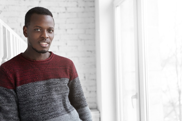 Séduisante jeune homme à la peau sombre vêtu d'un pull en jersey ayant un regard joyeux et joyeux