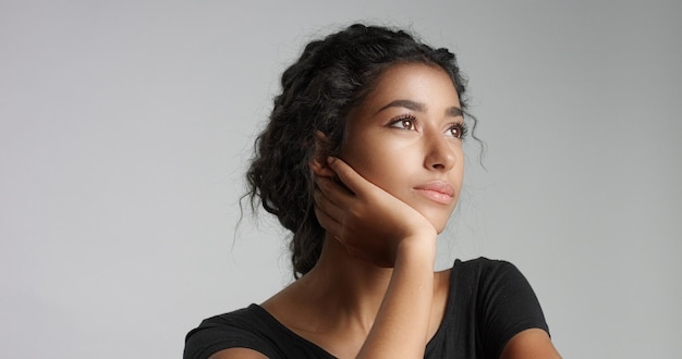 Séduisante jeune mannequin du Moyen-Orient touchant son joli visage avec une peau impeccable et souriante