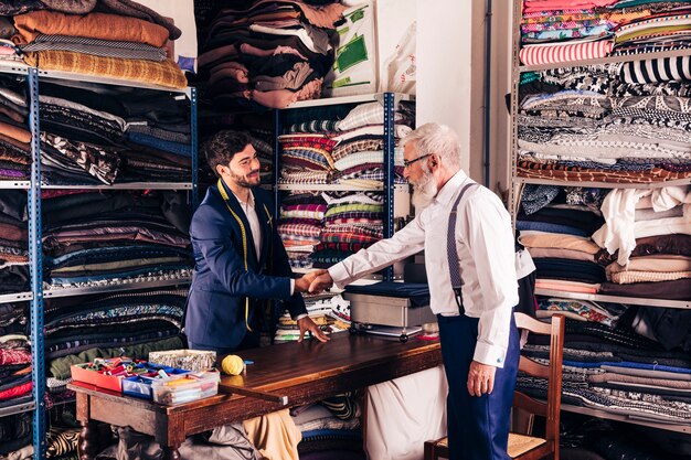 Senior client mâle serrant la main d&#39;un jeune tailleur masculin dans son atelier