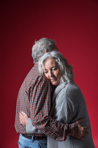 Senior couple embrassant debout sur fond rouge