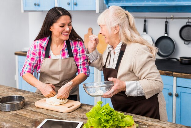 Senior femme appliquant de la farine sur le visage de la jeune fille préparant un repas dans la cuisine
