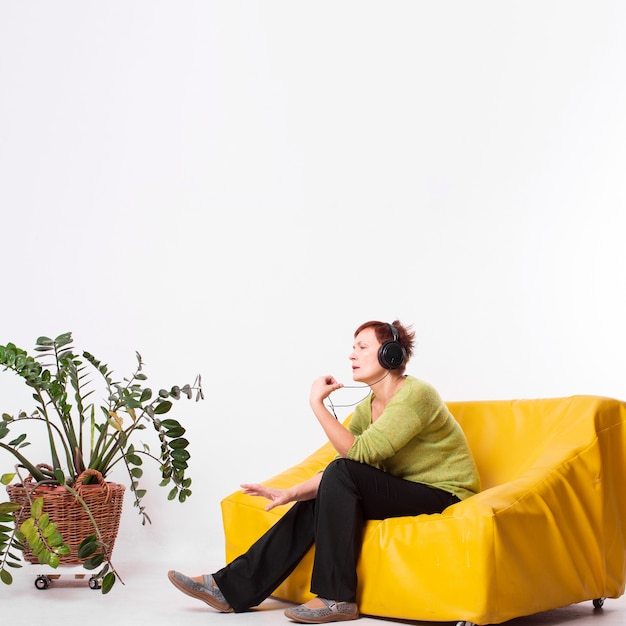 Senior femme assise sur un canapé et écoute de la musique