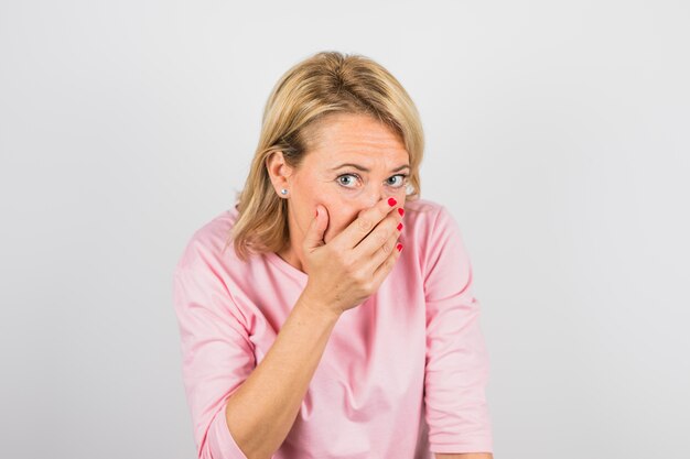 Senior femme en blouse rose fermant le visage à la main