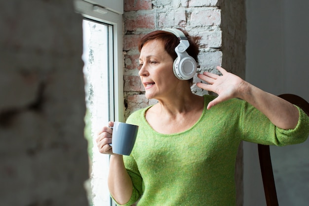 Senior femme écoutant de la musique et regardant sur la fenêtre